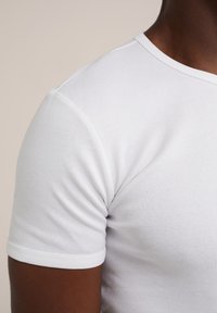 Weißes Baumwoll-T-Shirt mit kurzen Ärmeln und Rundhalsausschnitt. Besitzt eine glatte Textur und ein tailliertes Design.