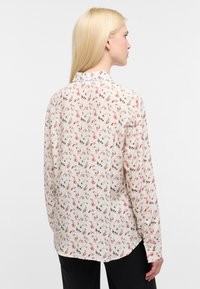Blusa a maniche lunghe in tessuto crema con un motivo colorato di figure. Presenta un colletto e un orlo curvo sul retro, con polsini abbottonati.