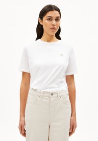 Witte t-shirt met korte mouwen en een ronde hals, versierd met een kleine geborduurde bloemenmotief op de linkerkant van de borst, in combinatie met lichtbeige broek.