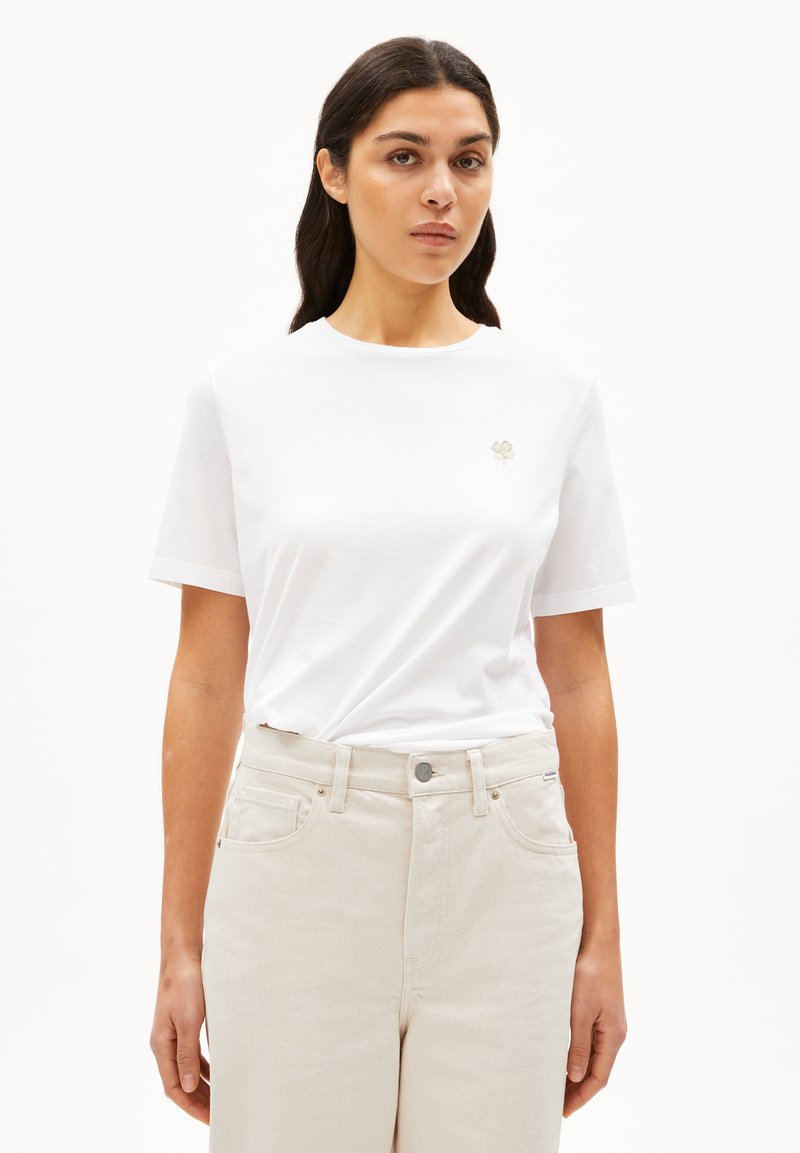 Witte t-shirt met korte mouwen en een ronde hals, versierd met een kleine geborduurde bloemenmotief op de linkerkant van de borst, in combinatie met lichtbeige broek.