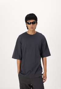 Sort oversized T-shirt med korte ærmer og rund halsudskæring. Bæres med moderne sorte solbriller for et moderne look.