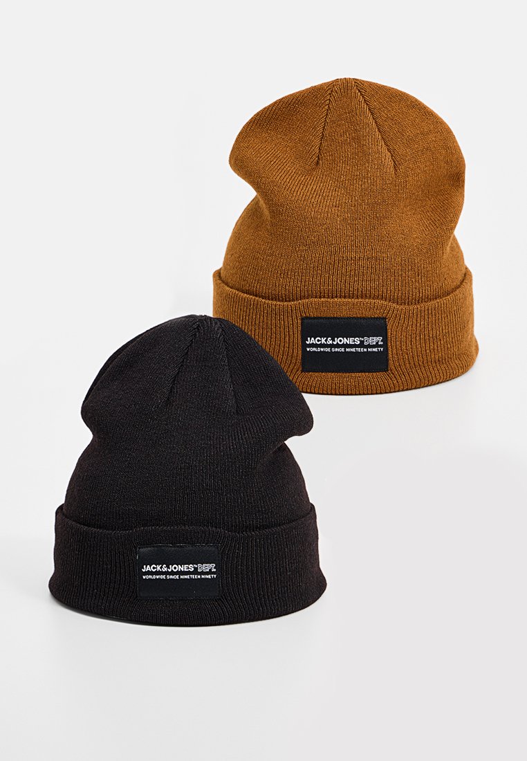 Twee beanie mutsen: één in donkerbruin, één in zwart. Beide hebben een geribbeld textuur en een merkpatch op de opgevouwen rand.