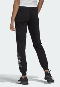 Svarta sweatpants med tapered design, elastisk midja och tre vita Adidas-logotyper på vänster ben. Tillverkade av mjukt bomullstyg.