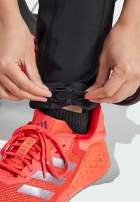 Scarpe da sport con una parte superiore in rete rossa texture, tre strisce argento e una suola spessa. Pantaloni sportivi neri con polsini regolabili vengono stretti.