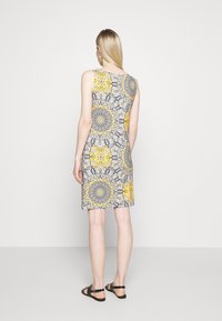 Robe sans manches présentant un motif floral en jaune, noir et gris. Fabriquée dans un tissu à la texture lisse, s'arrêtant juste au-dessus du genou.