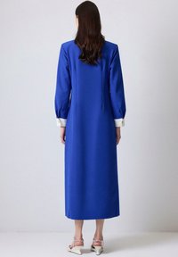 Long blue dress with a straight design and puff sleeves. Features contrasting white cuffs and a smooth texture.