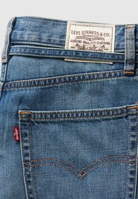 Poche arrière d'un jean en denim bleu avec un écusson en cuir Levi Strauss & Co. et une étiquette en tissu rouge Levi's sur la couture.