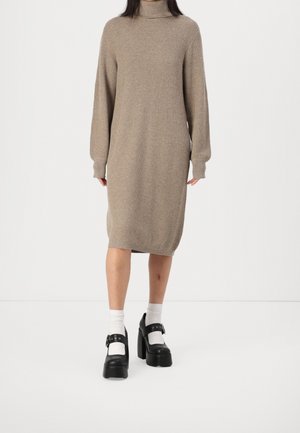 Woman wearing a beige ribbed long-sleeve midi sweater dress with white socks and black platform Mary Jane shoes.