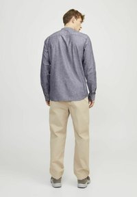 Camicia di chambray a maniche lunghe, di colore blu scuro, con colletto button-down, abbinata a pantaloni beige chiaro e sneakers grigie sportive.