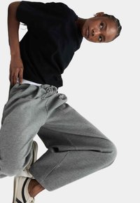 Schwarzes Kurzarm-T-Shirt mit Rundhalsausschnitt, kombiniert mit hellgrauen Sweatpants mit einer Kordelzugtaillierung und entspannter Passform. Sneaker in Beige und Marineblau.