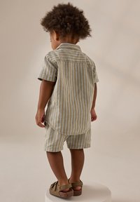 Conjunto de camisa de manga corta y pantalones cortos a rayas en beige claro y gris suave. Presenta rayas horizontales y verticales, dobladillo redondeado y bolsillos.