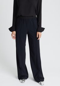 Zwarte wijde broek met een zachte textuur en geplooide details. Gecombineerd met een zwarte longsleeve top en metallic zilveren schoenen.