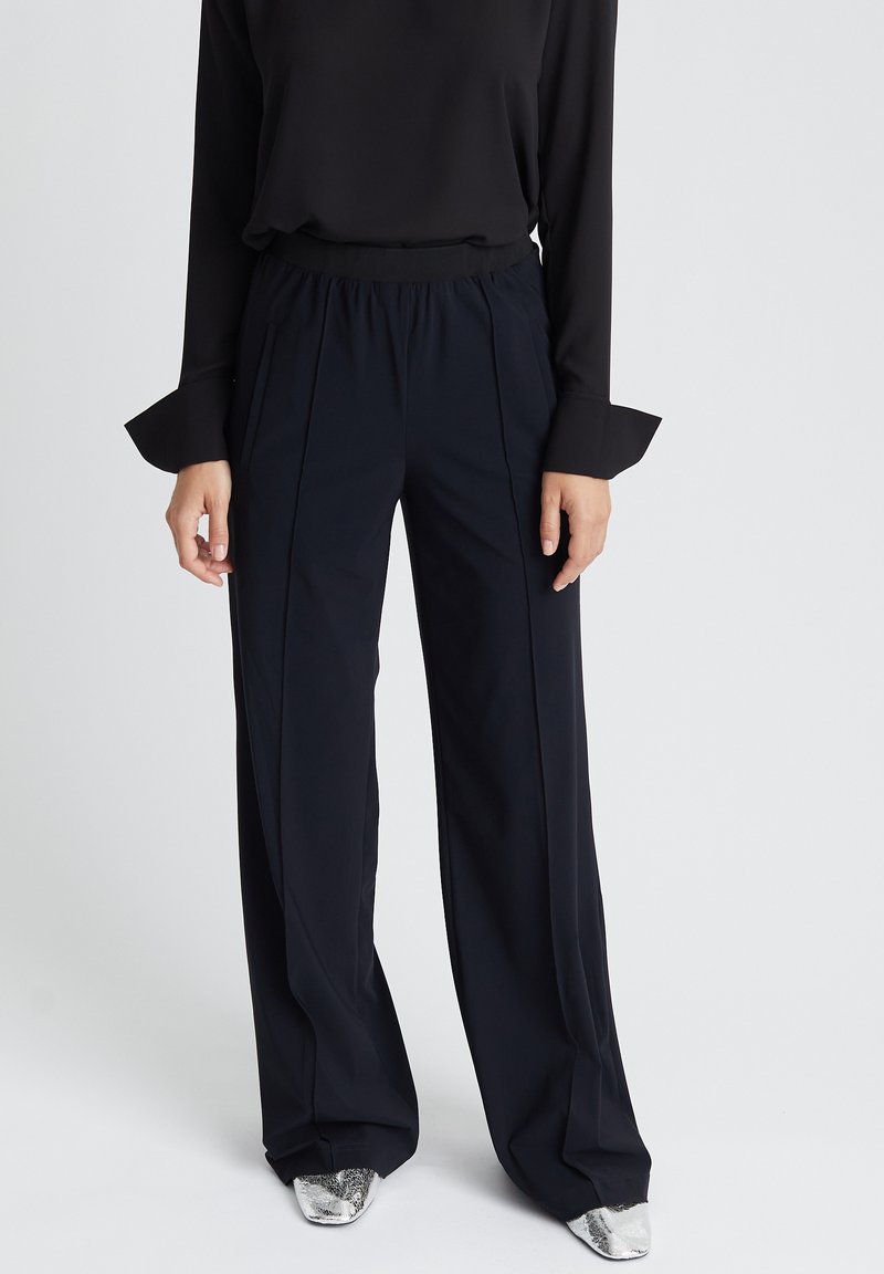 Zwarte wijde broek met een zachte textuur en geplooide details. Gecombineerd met een zwarte longsleeve top en metallic zilveren schoenen.