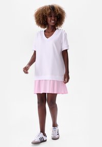Witte oversized V-hals T-shirt met korte mouwen, laag over een roze en witte gestreepte plooienrok. Draagt het met witte sneakers.