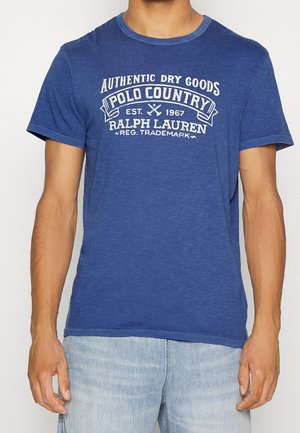 T-shirt en coton bleu avec un col rond et des manches courtes, arborant du texte blanc et un design graphique sur le devant.