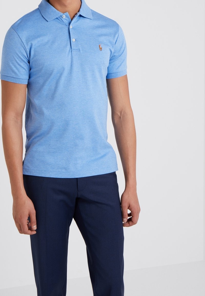 Polo bleu clair en coton doux, avec un col classique, des manches courtes et un petit logo brodé sur la poitrine. Associé à un pantalon marine.