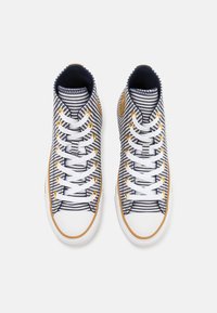 Zapatillas altas de lona a rayas en azul marino y blanco, con cordones blancos, ojales dorados y una suela de goma con un acento de color marrón.