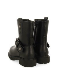 Botas de tobillo de cuero negro con un acabado mate, que presentan un cierre lateral con cremallera, detalle de hebilla y acentos de tachuelas en la parte trasera. Suela de goma texturizada.