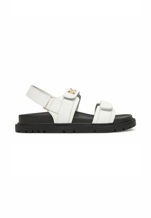Hvid sandal med to justerbare stropper og en sort tyk sål, vist fra siden på en hvid baggrund.