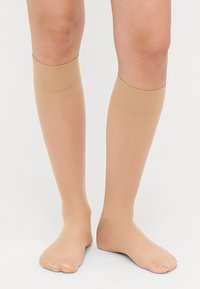 Kniehoge compressiekousen in een huidskleur, gemaakt van een glad, doorschijnend materiaal, met gestructureerde banden aan de bovenkant voor een veilige pasvorm.
