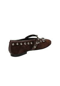 Scarpa piatta in suede marrone con punta a forma appuntita, decorata con borchie argentate lungo il lato e una sottile cinturino alla caviglia. Suola piatta in gomma.