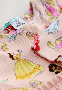 Vaaleanpunainen kangas, jossa on erilaisia värisiä Disney-prinsessoja; ribbitekstuuri; tarrassa lukee "Disney PRINCESS". Yksityiskohtainen kuvio koko pinnalla.