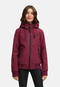 Burgunderrød hettejakke med glidelås foran, to sidelommer og ribbestrikkede mansjetter. Har snorer for justering og et teksturert stoff.