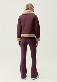 Bordová bunda s béžovým kožichovým límcem a manžetami, s krátkým střihem. Nosená s ladícími bordovými zvonovými kalhotami a bílými teniskami.