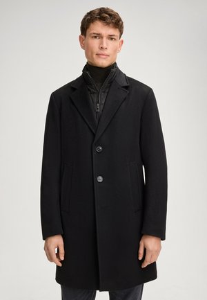 Zwarte jas van een wollen mix met een klassiek ontwerp, twee knopen, gegoten revers en zijzakken, gedragen over een zwarte zip-up jack.