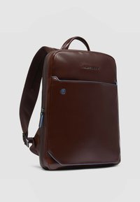 Zaino in pelle marrone con una texture liscia, chiusura a zip, tasca frontale con accento blu e spallacci imbottiti e regolabili.