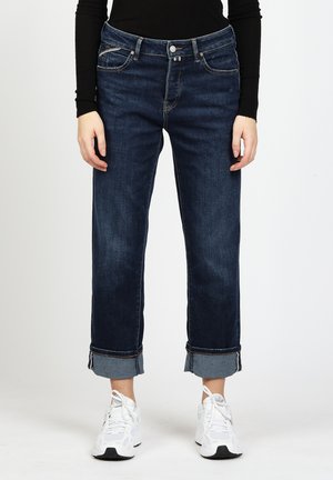 Dark denim jeans with a straight-leg design, rolled cuffs, and five-pocket style. Worn with white athletic shoes. Smooth texture.
