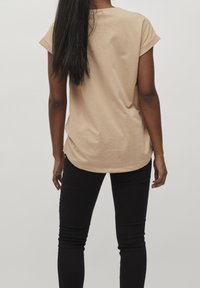 Beige kortärmad T-shirt med rundad nederkant, tillverkad av mjukt tyg, ihopparad med svarta åtsittande jeans. Inga synliga mönster eller grafik.