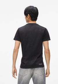 Melna kokvilnas T-kreklu ar apaļu kakla izgriezumu, īsajām piedurknēm un vienkāršu dizainu. Aizmugurē ir neliels balts logo pie apakšmalas.