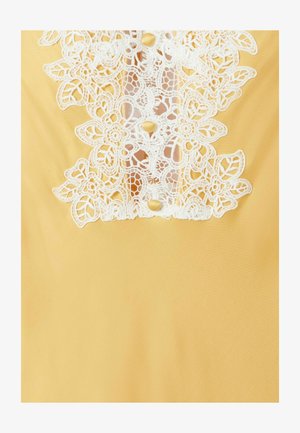 Tessuto giallo con bordo in pizzo floreale bianco e tre piccoli bottoni gialli al centro.