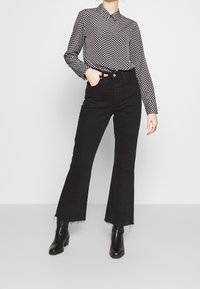 Black flared jeans with raw hems paired with a black and white checkered button-up shirt featuring a collar. Worn with black ankle boots.