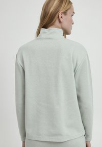 Pull léger vert clair avec un col haut, en tissu doux et texturé. Il possède des manches longues et une coupe décontractée. Vue arrière présentée.