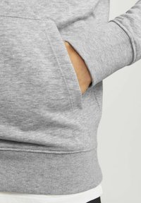 Grauer Sweatshirt mit weicher Textur, gerippten Bündchen und einer Taschenaufschrift auf der Vorderseite. Es verfügt über ein schlichtes Design mit minimalen Akzenten.