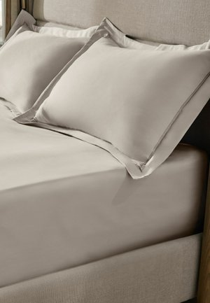 Neutrales beiges Spannbettlaken und passende Kissenbezüge auf einem Bett mit einem gepolsterten Stoffkopfteil.