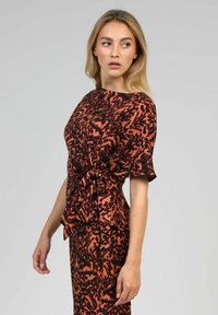 Haut à manches courtes dans un motif abstrait orange et noir, avec une taille cintrée et un ourlet en couches à volants. Tissu lisse avec un léger éclat.