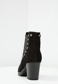 Czarne zamszowe botki za kostkę z grubym obcasem i srebrnymi ćwiekami wzdłuż boku, blisko elastycznej wstawki dla łatwego zakładania.
