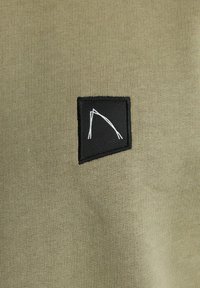 Tessuto verde oliva con una superficie liscia caratterizzato da una patch nera. La patch presenta dettagli in linea bianca con un design astratto.