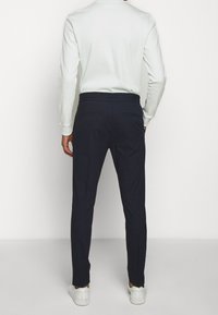 Navy trousers featuring a stretchy waistband, tapered fit, and back pockets, paired with a light-colored long-sleeve top.