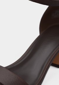 Σκούρο καφέ σανδάλι ανοιχτού δακτύλου με χαμηλό τακούνι τύπου block και μια μόνο λωρίδα πάνω από τα δάχτυλα, εμφανίζεται σε λευκό φόντο.