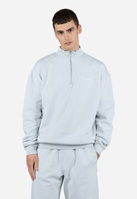 Lyseblå fleece zip-up sweatshirt med høj krave, ribbede ærmer og kant, der har et lille logo på brystet. Blød tekstur og afslappet pasform.