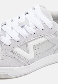 Grå semsket sneakers med hvite mesh-detaljer, hvite lisser og en hevet hvit logo. Har perforerte detaljer og en teksturert såle.