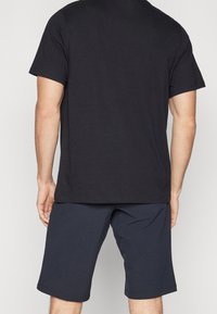 Homme portant un t-shirt noir uni à manches courtes et un short bleu marine foncé arrivant au genou, vu de dos.