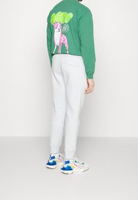 Green long-sleeve t-shirt with pink dog graphic and text on the back, paired with light gray joggers and colorful athletic shoes.