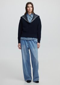 Maglione a maglia blu navy con un ampio colletto decorato, tre bottoni e orlo a coste, abbinato a pantaloni in denim a gamba larga di un blu chiaro.