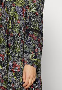 Vestido com padrão floral sobre fundo preto, apresentando flores verdes, vermelhas e roxas. Mangas elásticas e detalhe de design franzido.