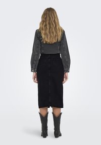 Jupe en denim noir avec une coupe mi-longue, assortie à une chemise à manches longues gris foncé. Portée avec des bottes de cowboy noires présentant des détails uniques.